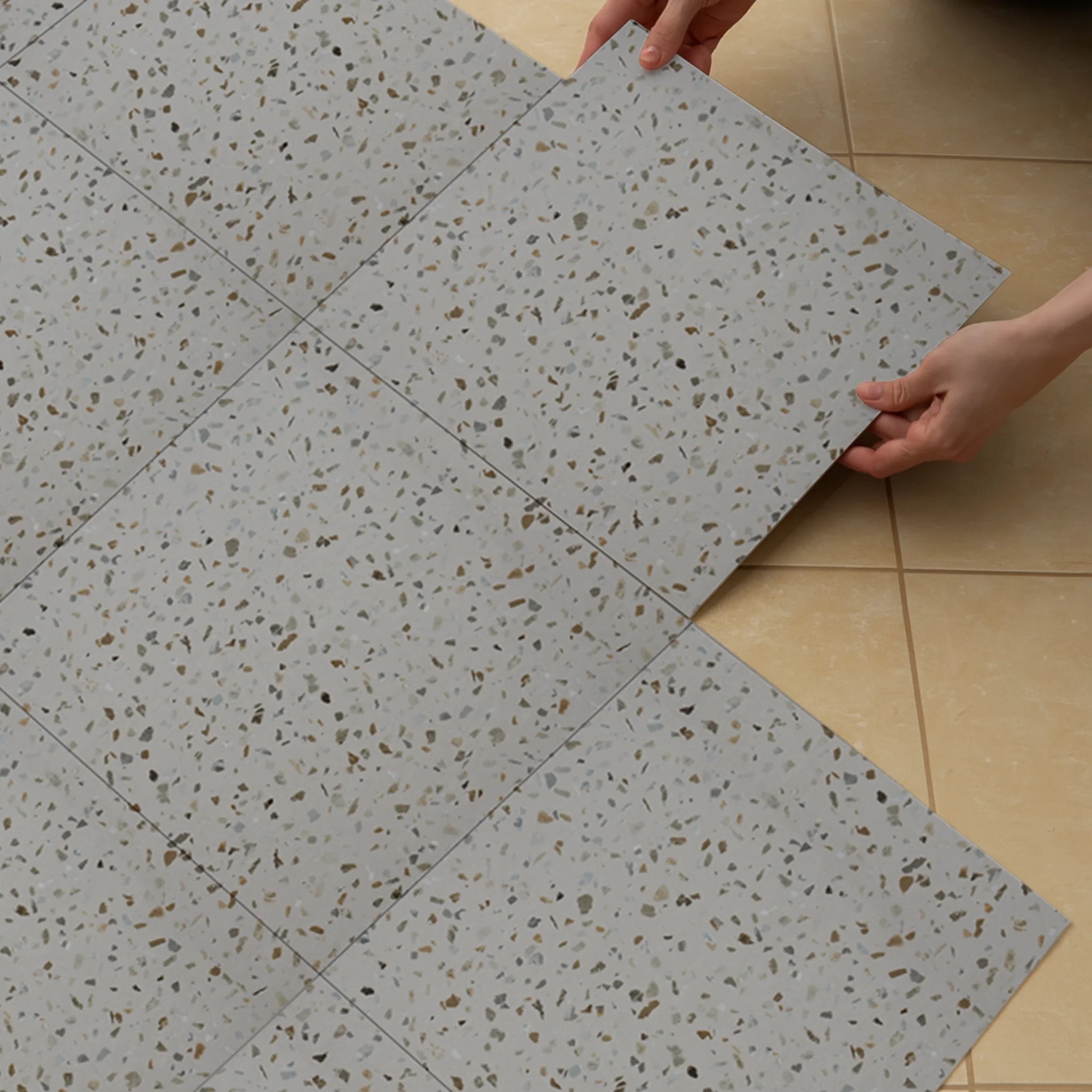 A person installing a self-adhesive tile over a tile floor