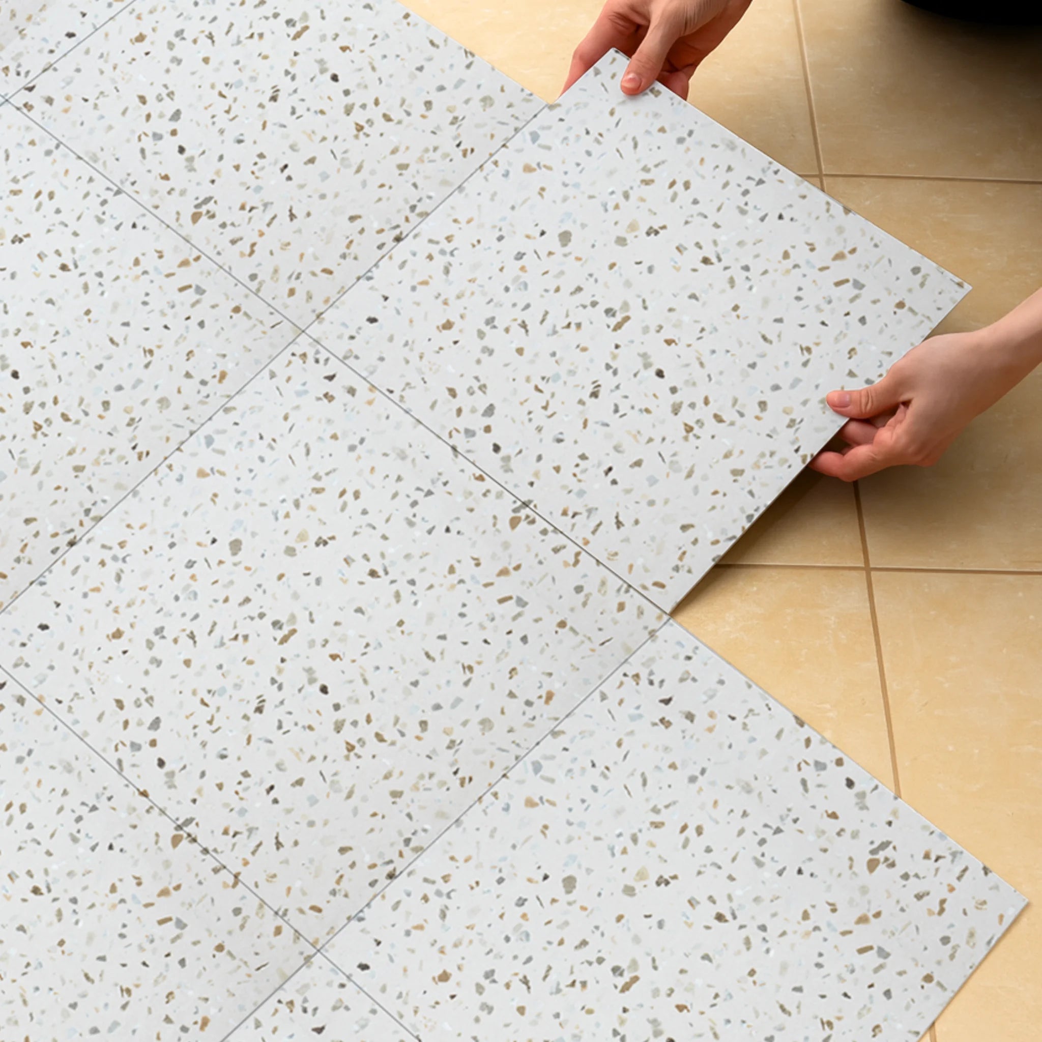 A person installing a self-adhesive tile over a tile floor