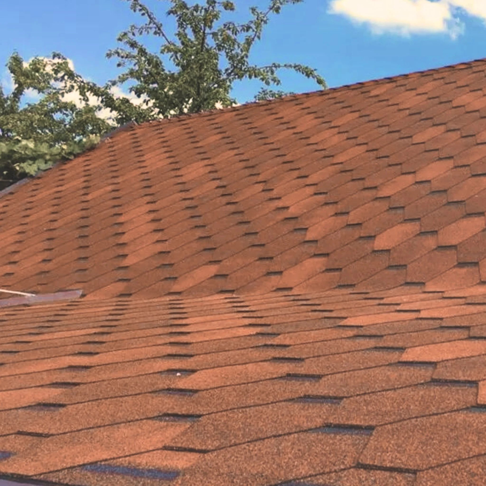 roof with installed brown hexagonal shingles against blue sky