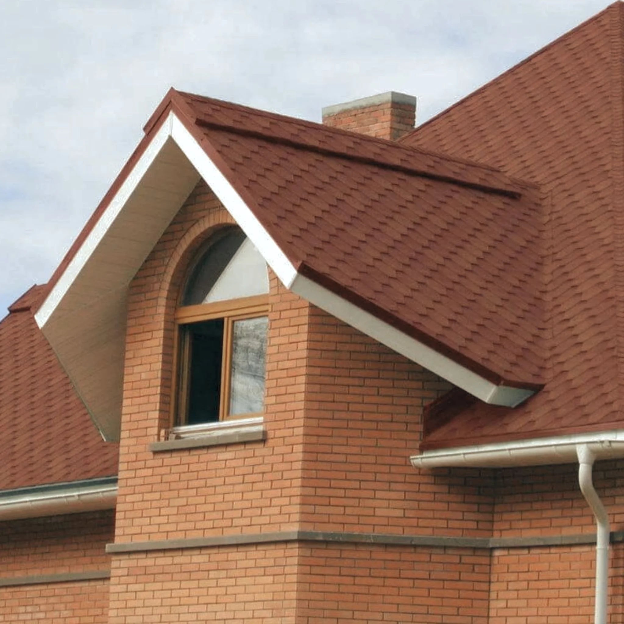 brick house with brown shingle roof under blue sky