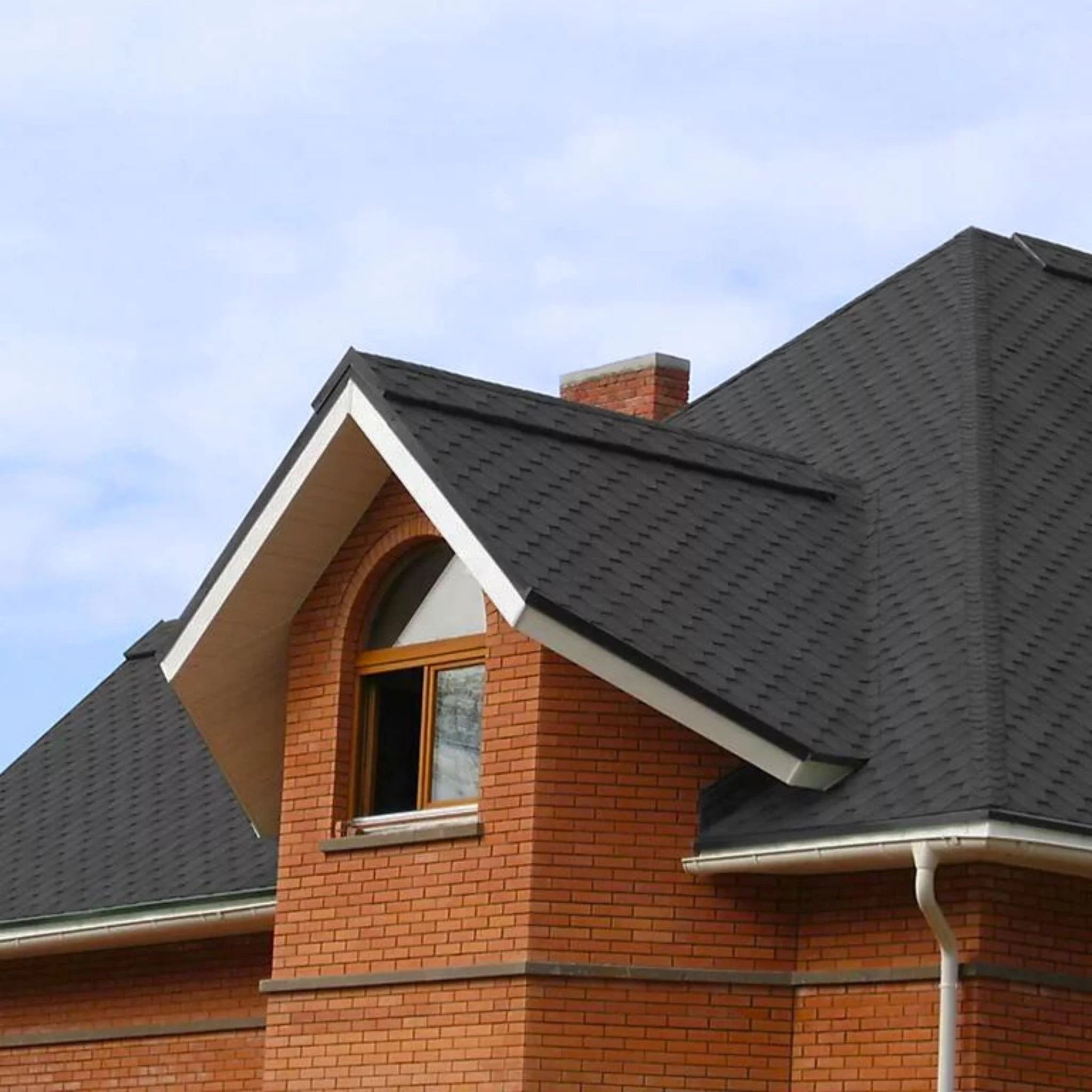 brick house with graphite shingle roof under blue sky