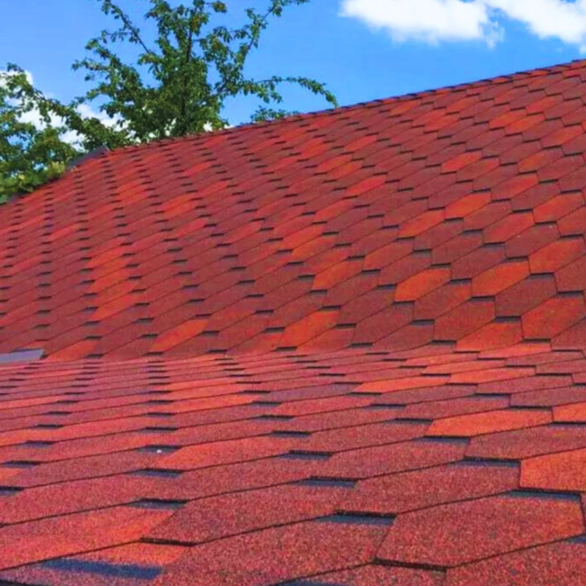 roof with installed red hexagonal shingles against blue sky