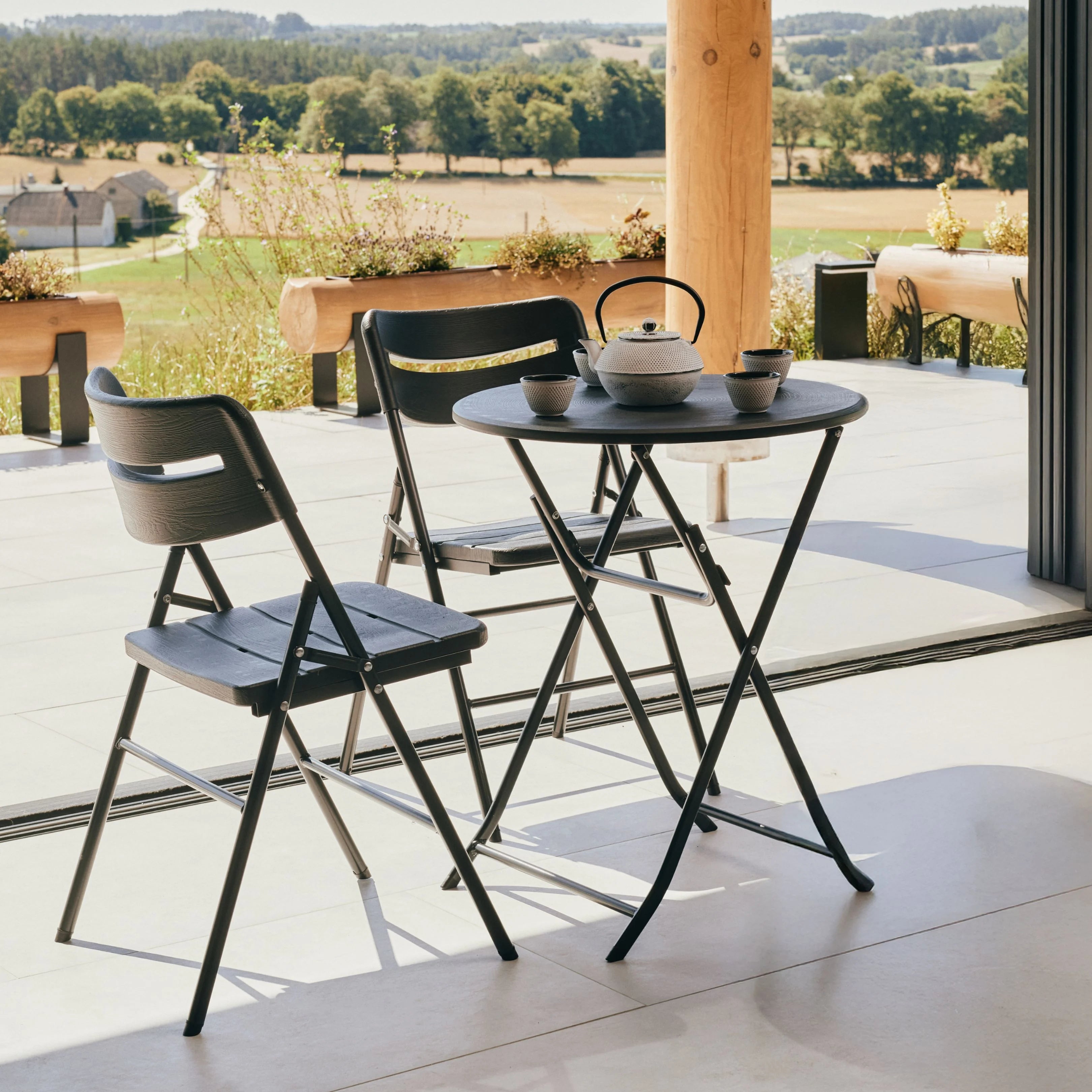 black round folding table and chair on patio with flower vase