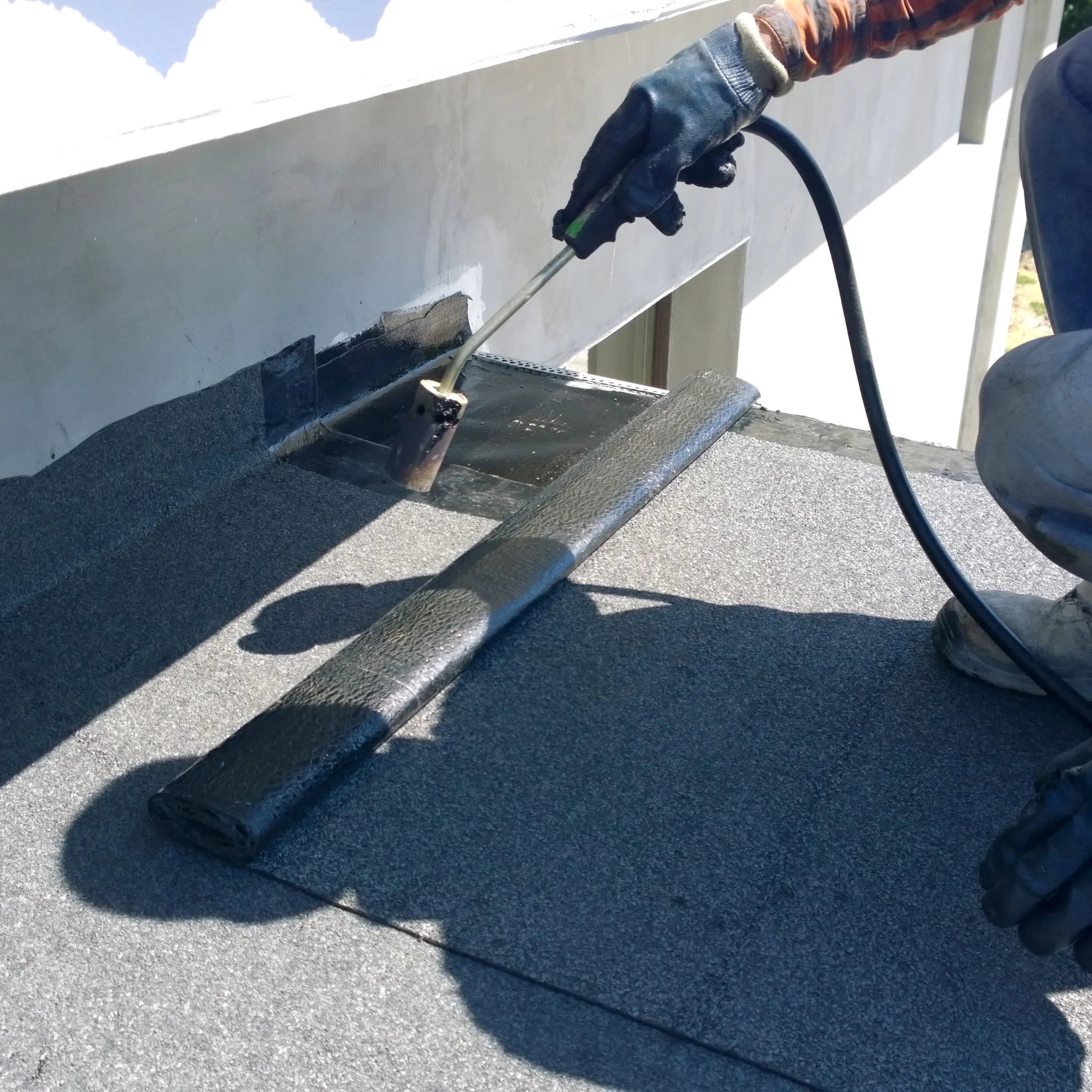 worker applying cap sheet to flat roof using heat tool